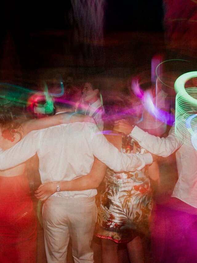 Invitados bailando y riendo durante la celebración de boda con luces cálidas.