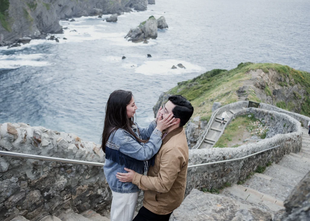 Pedida de mano en San Juan de Gaztelugatxe | Fotógrafo en Bilbao 8 La emoción de una pedida de mano en San Juan de Gaztelugatxe
Fotografiar una pedida de mano es muy diferente a fotografiar una sesión de pareja.
Hay algo que cambia completamente.
La sorpresa.
Como fotógrafo, tienes que estar pendiente de muchas cosas al mismo tiempo: la luz, el entorno, las personas que pasan, la posición de la pareja y, sobre todo, ese pequeño instante en el que todo cambia.
Pero también hay que saber desaparecer.
No dirigir demasiado.
No convertir un momento íntimo en una sesión de fotos.
Simplemente observar.
Esperar.
Y estar preparado.
En una pedida de mano, muchas veces la fotografía más importante no es la que muestra el anillo.
Es la que muestra la reacción.
La mirada.
La sorpresa.
La sonrisa que aparece sin pensar.
Ese segundo en el que una persona entiende lo que está pasando y el resto del mundo parece desaparecer.